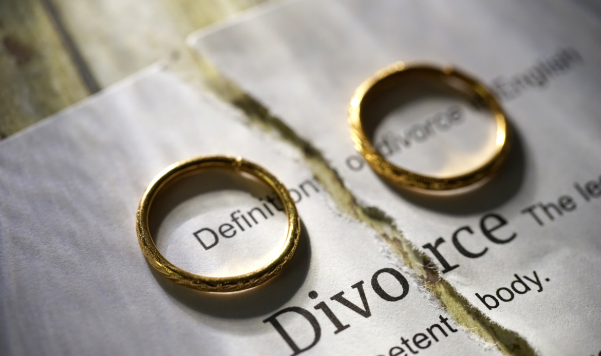 Two gold wedding rings placed on a torn divorce document, symbolizing separation and the end of a marriage.