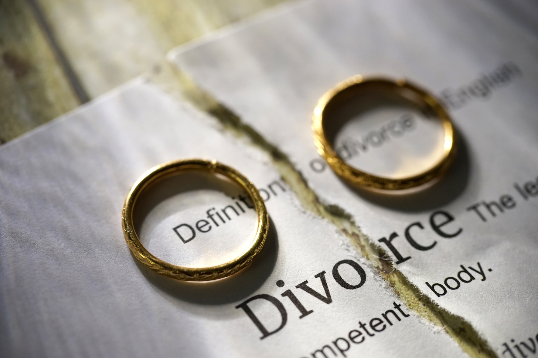 Two gold wedding rings placed on a torn divorce document, symbolizing separation and the end of a marriage.