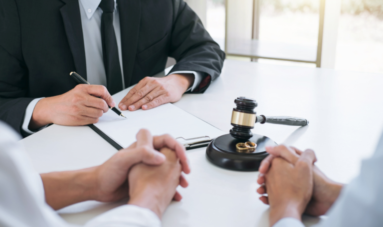 A lawyer reviewing documents with a couple during an uncontested divorce consultation, with a gavel and wedding rings on the table.