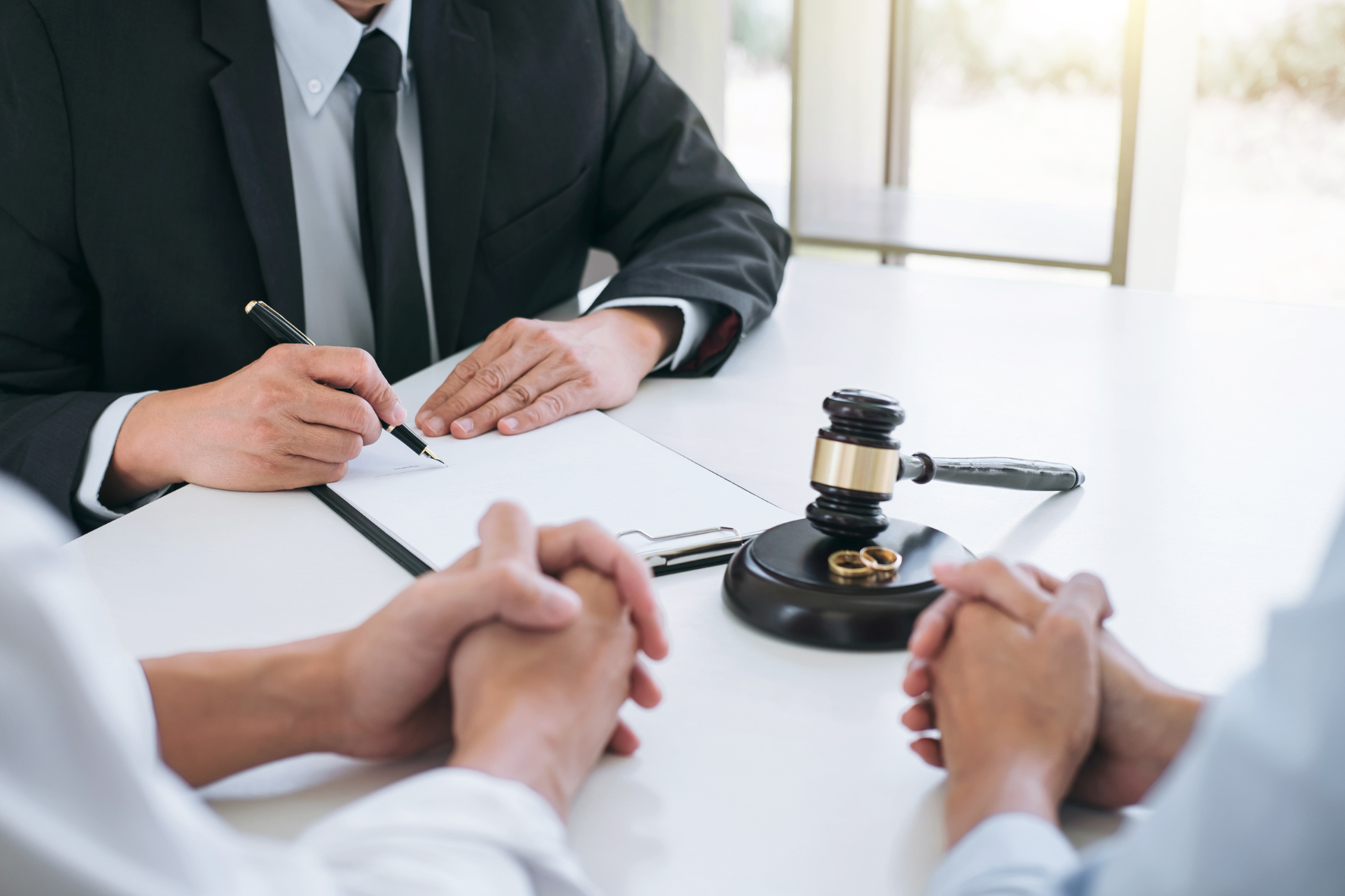 A lawyer reviewing documents with a couple during an uncontested divorce consultation, with a gavel and wedding rings on the table.