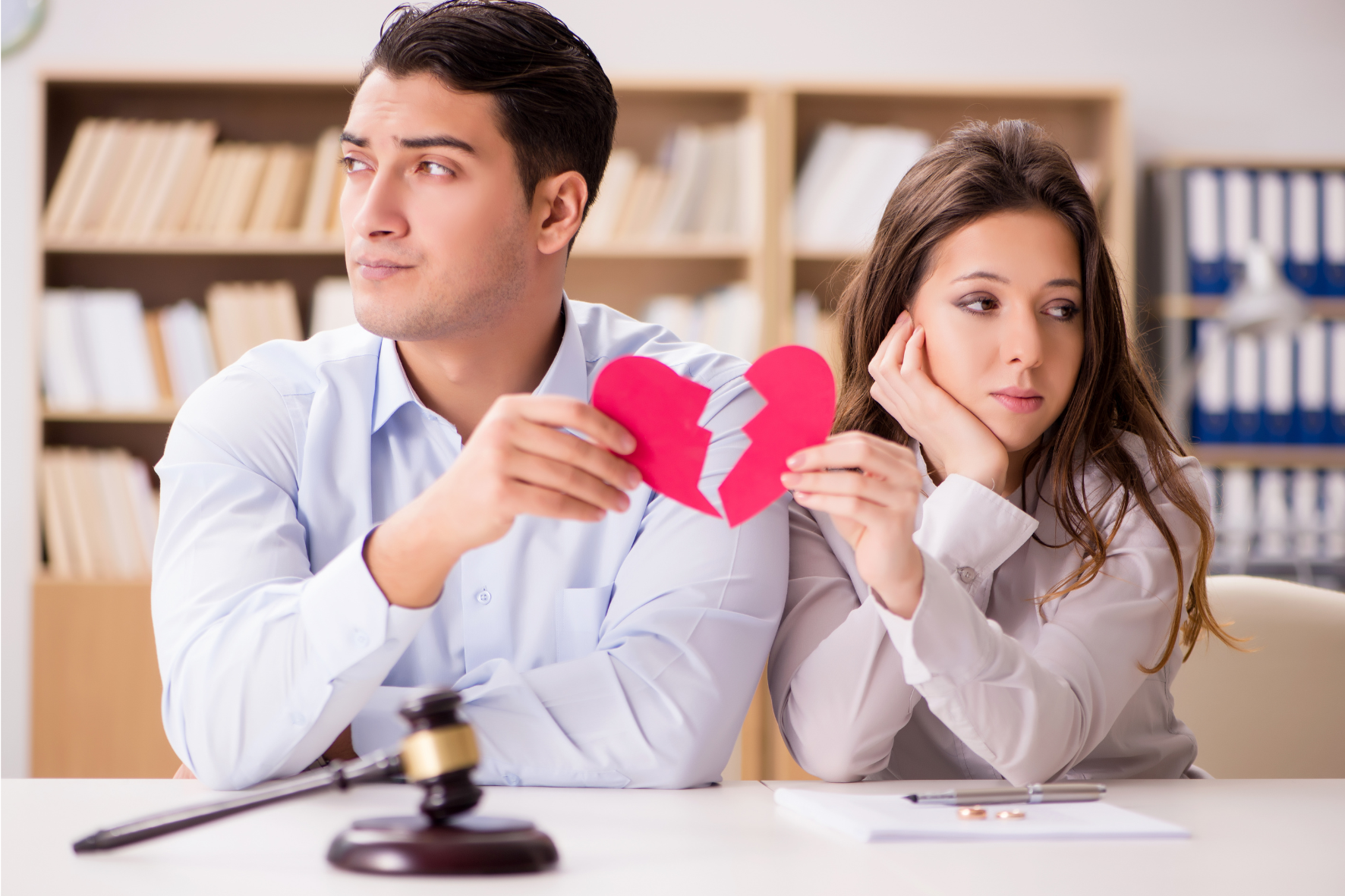 A couple holding a broken heart cutout during a divorce consultation, with a gavel and paperwork on the table, symbolizing the divorce process in Canada.