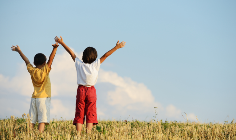 Two children standing in a field with arms raised, symbolizing happiness, stability, and a bright future in child custody decisions.